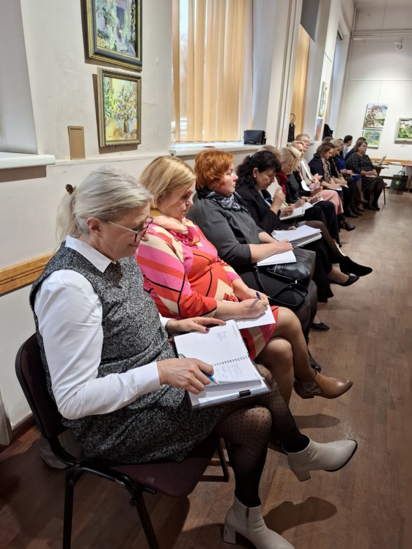 Semināra norise — dalībnieki sēž uz krēsliem zālē, skatās dokumentus