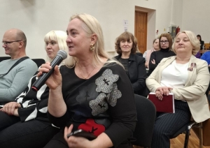 Semināra norise — sieviete ar mikrofonu sēž uz krēsla