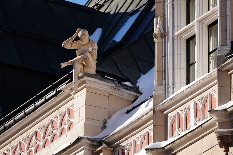 Foto: Amatu iela 4, bilde kur uz ēkas sēž statuja vīrieša skulptūra