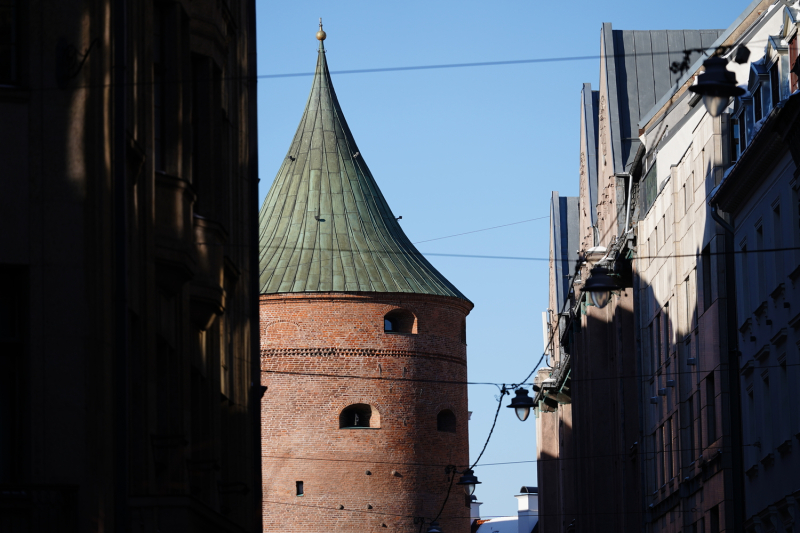 Foto redzams Rīgas Pulvertornis apspīdēts saulē, un skats caur mājām