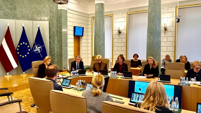 demogrāfiskās lietu padomes sapulcē cilvēki sēž pie galdiem un apspriež.