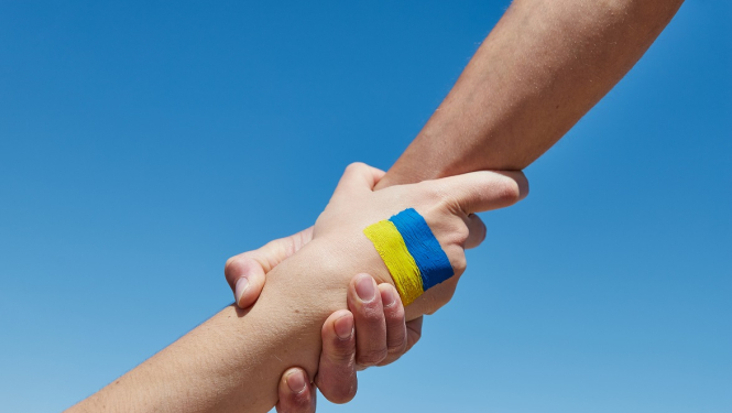 Sociālā palīdzība ukraiņiem, divas rokas sadevušās un uz vienas attēlots Ukrainas karogs