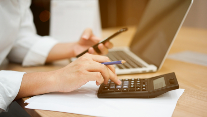 attēlots ka cilveks sēž pie galda, atvēris datoru, skaita kalkulatora un rēķina