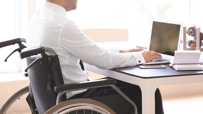 cilveks invaliditates kreslina pie datora strada, attēlo ka cilveki ar invaliditāti arī var strādāt darbā