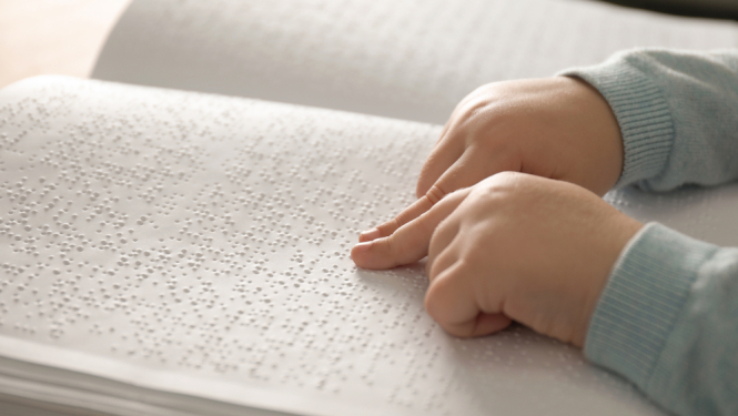 cilvēkam ar redzes traucējumiem grāmata, kuru lasa bērns