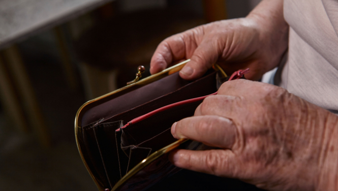 Gados vecāka cilvēka rokas atver tukšu maku ar rāvējslēdzēju, uzsverot finanšu trūkumu vai grūtības.