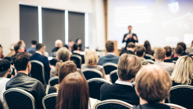 cilvēki sēž konferencē, cilvēki no mugurpuses redzami