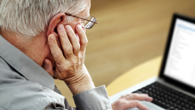 vecā cilvēka portrets no aizmugures, kurš sēž pie datora un strādā