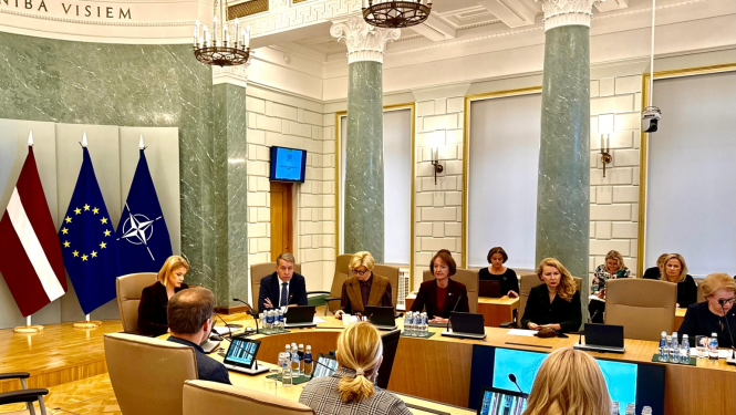 demogrāfiskās lietu padomes sapulcē cilvēki sēž pie galdiem un apspriež.