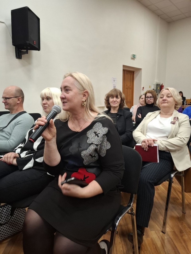 Semināra norise — sieviete ar mikrofonu sēž uz krēsla